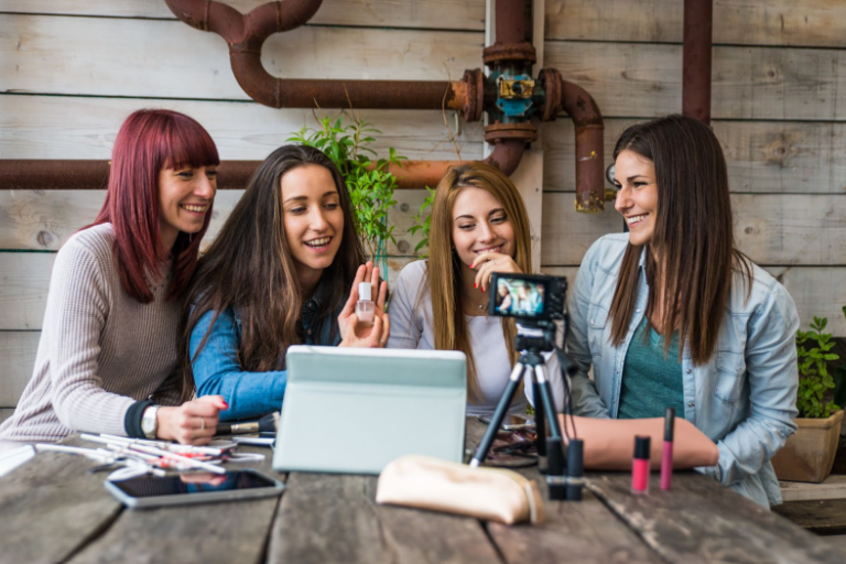 4 nasmejane devojke okupljene oko tableta i telefona kreiraju sadržaj za društvene mreže - influencer marketing